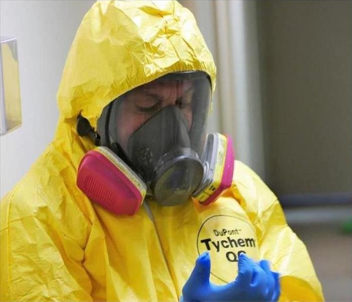 Man in protective gear and face masks in front of a SERVPRO truck