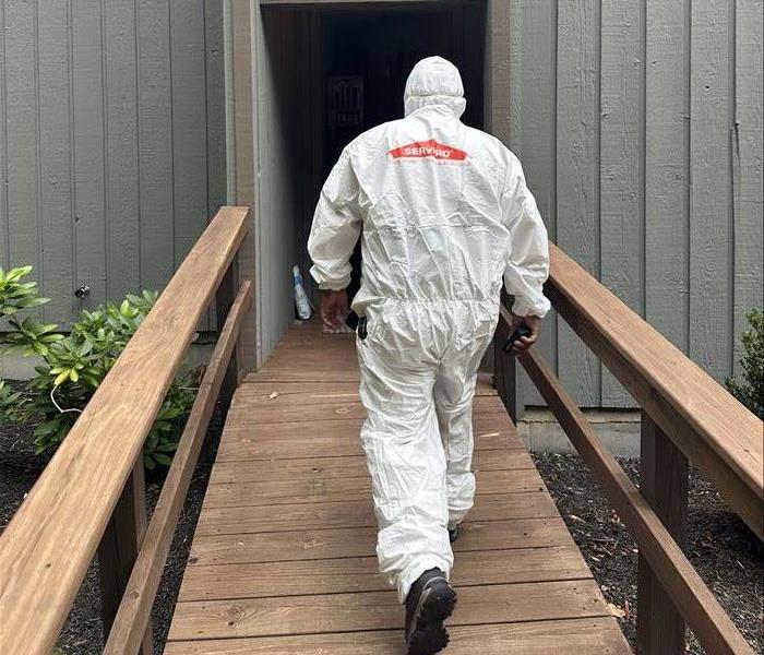 man in protective gear with servpro logo walking into a home